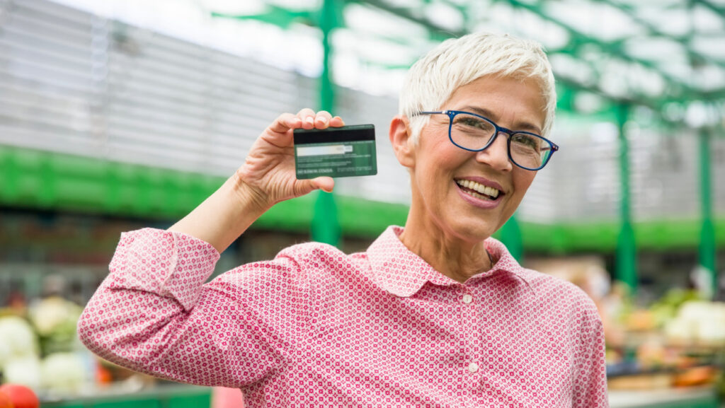 赤いシャツの女性がクレジットカードを手に笑っている写真