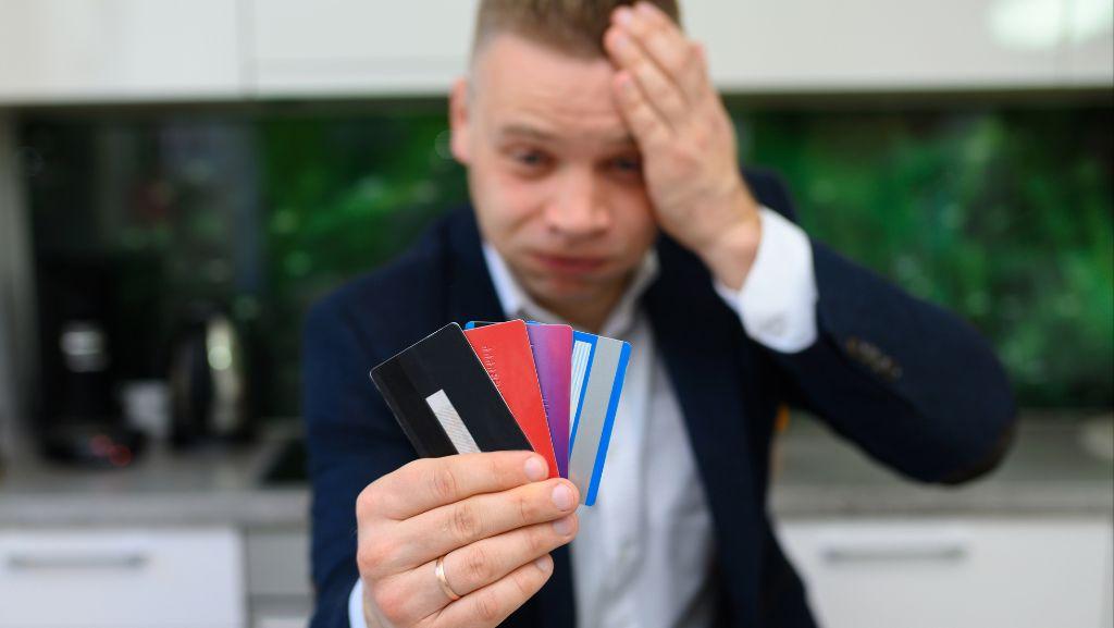 4枚のクレジットカードを手にして頭を抱える男性の写真
